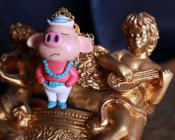 A close up of a toy pig on top of a gold statue.