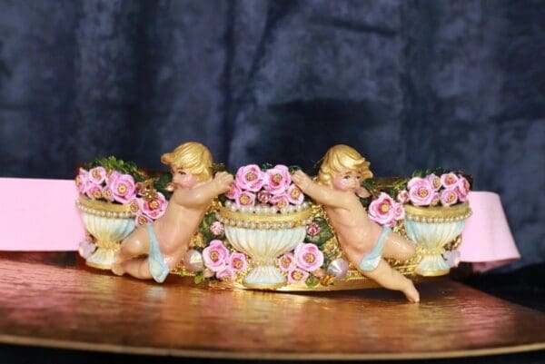 A table with three cherubs and pink flowers.