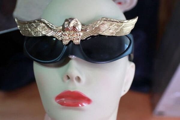 A mannequin head wearing sunglasses and a gold eagle.