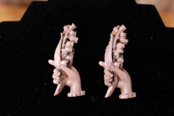 A pair of white earrings with arms and hands.