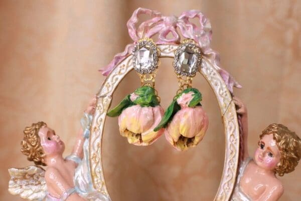 A pair of earrings hanging from the side of a pink bow.