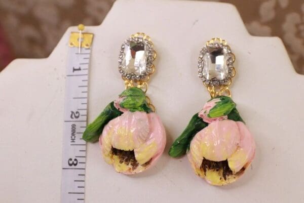 A pair of earrings with pink flowers and green leaves.