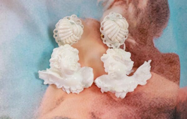 A pair of white earrings on top of a pink and blue background.