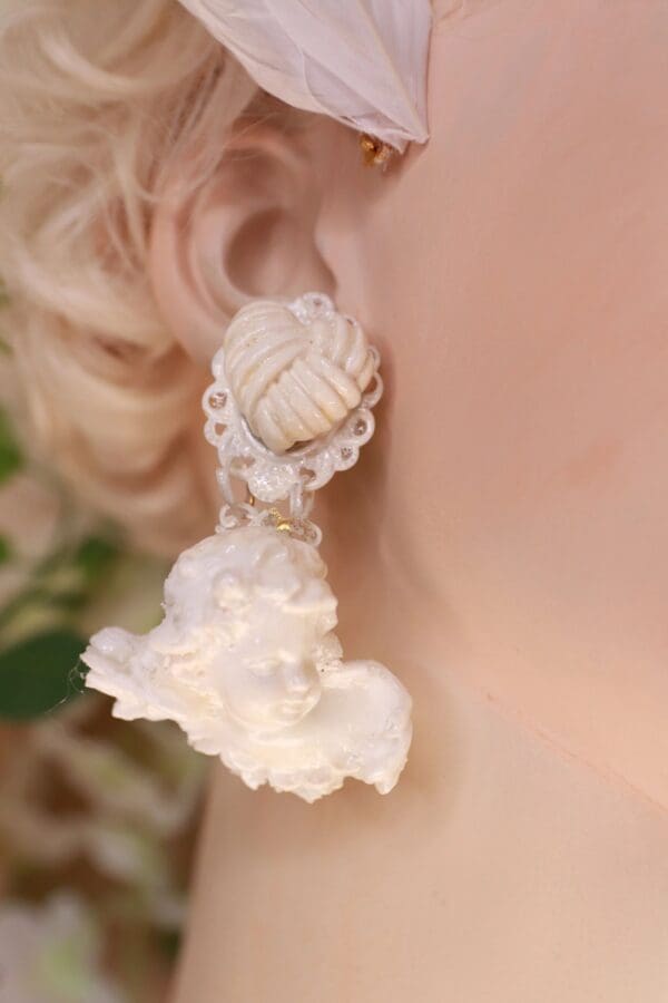 A woman wearing white earrings with flowers hanging from them.