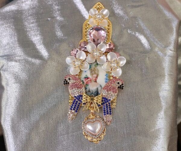 A gold and white brooch with pink, blue and yellow beads.