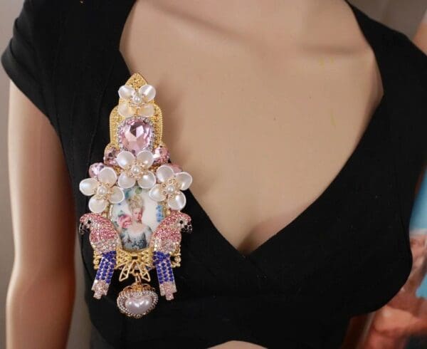 A woman wearing a black top and a pink and blue brooch.