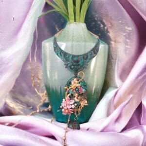 A vase with a necklace on it sitting in front of a pink cloth.