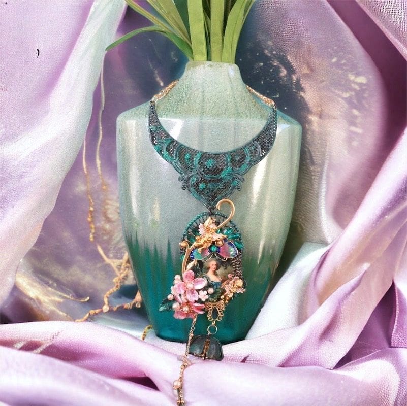 A vase with a necklace on it sitting in front of a pink cloth.