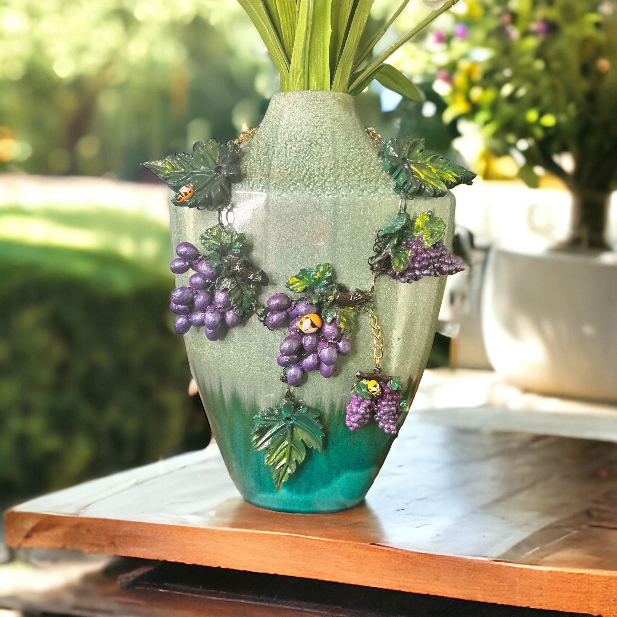 A vase with grapes on it sitting on top of a table.