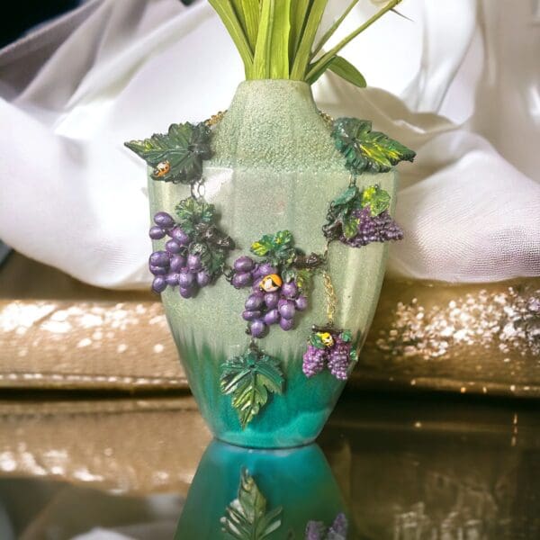 A vase with grapes on it sitting on top of a table.