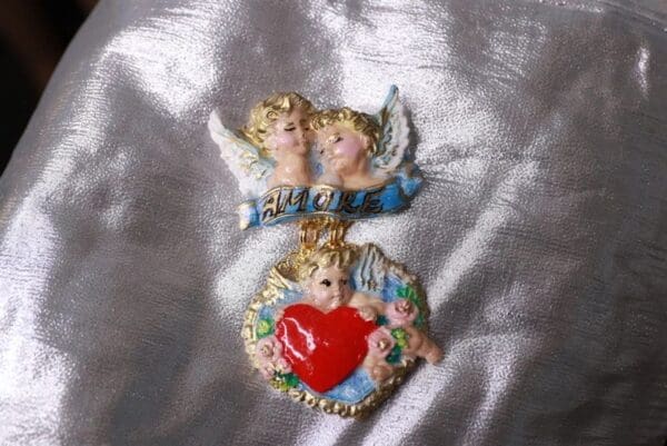 Two angels are holding a heart on the back of a bow.