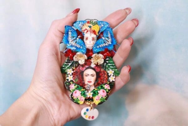 A person holding a colorful brooch with frida kahlo on it.