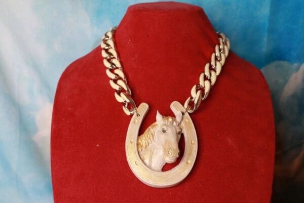 A horse head necklace on a red display stand.