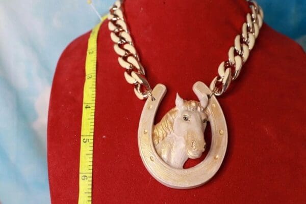 A horse head necklace on a chain with a measuring tape.