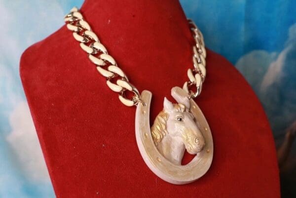 A horse head and chain necklace on a red velvet display.