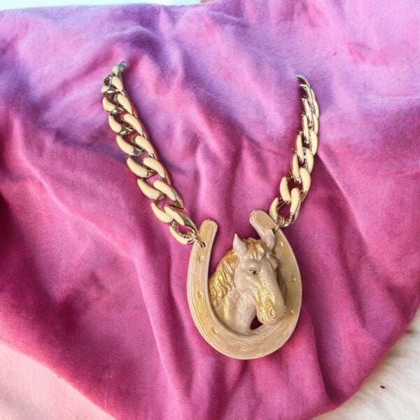 A horse head necklace on top of pink fabric.
