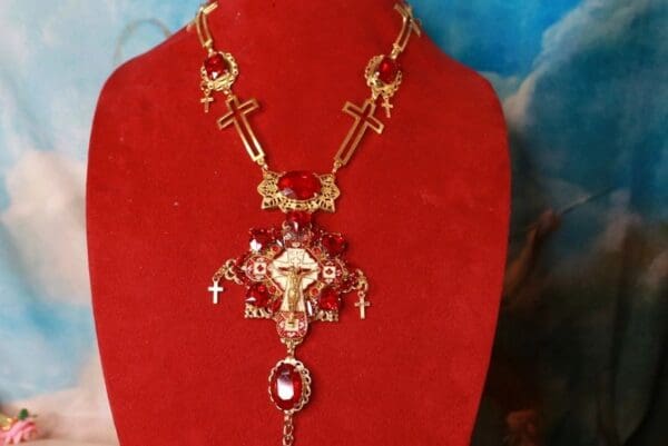 A red necklace with crosses and other jewelry on it.