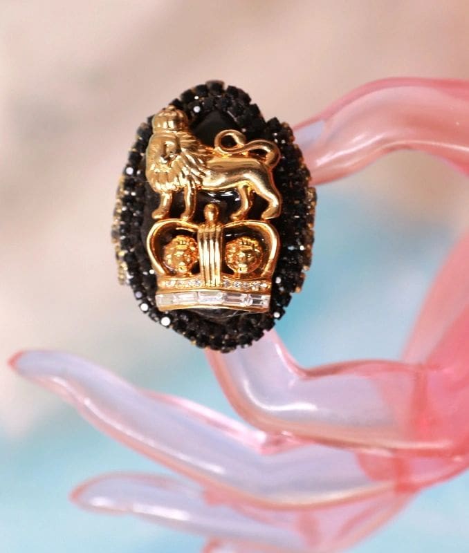 A gold and black ring sitting on top of a pink glass.