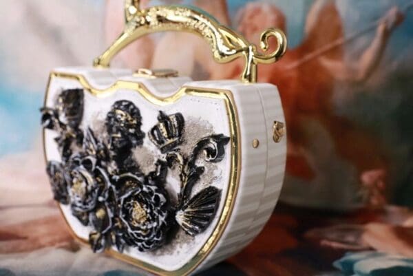A white purse with gold handle and flowers on it.