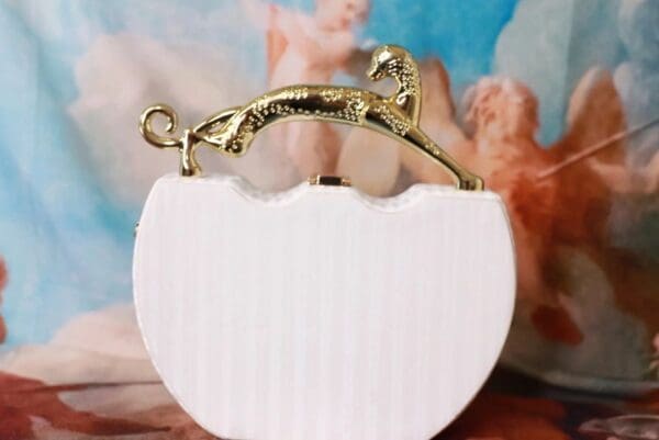 A white purse with gold handle and a picture of an angel.