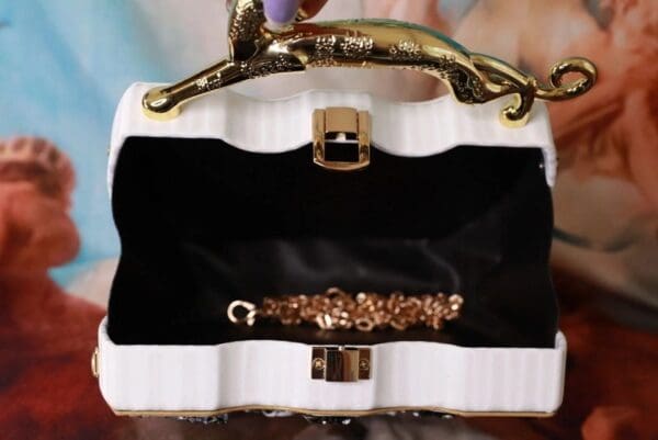 A white purse with gold cat handle and black lining.