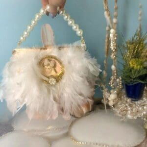 A white purse with feathers and pearls on top of the bag.