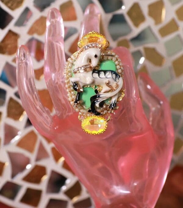 A pink hand with a green and white ring on it