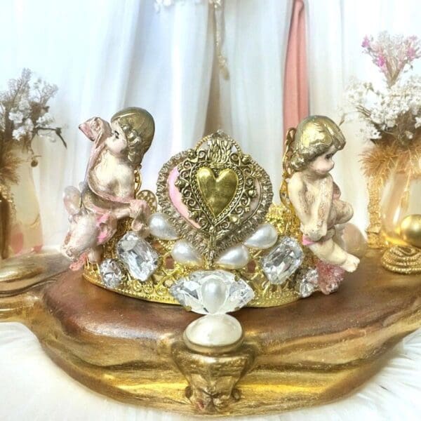 A gold crown with two angels sitting on it.