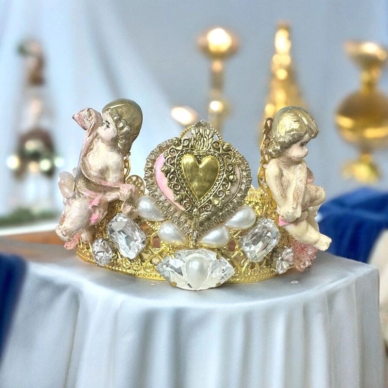 A gold and white crown with two angels on top of it.