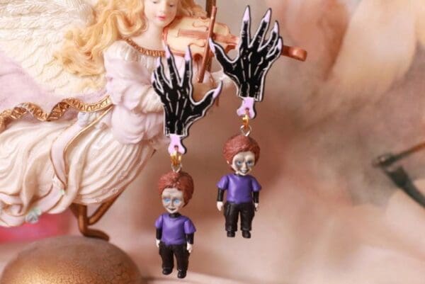 A pair of earrings with a skeleton hand and a boy.
