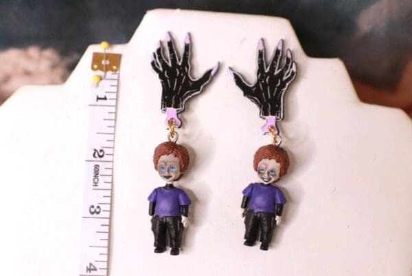 A pair of earrings with the shape of a skeleton hand and a boy.