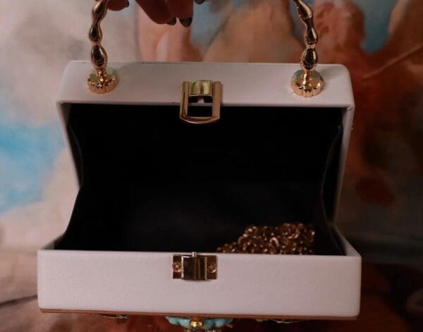 A white purse with gold chain handles and a small opening.