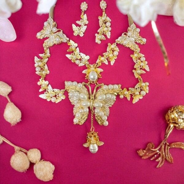 A butterfly necklace and earrings set on pink background.