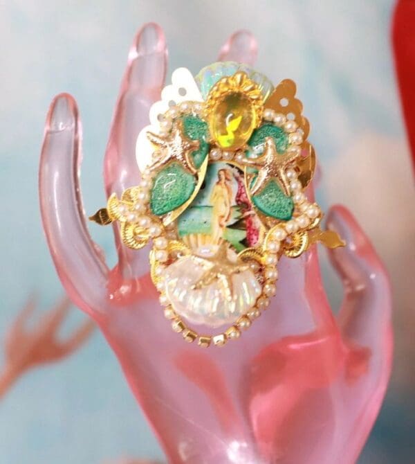 A hand holding a ring with a flower on it.