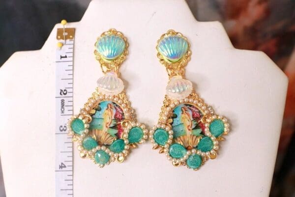 A pair of earrings with shells and mermaids on them.