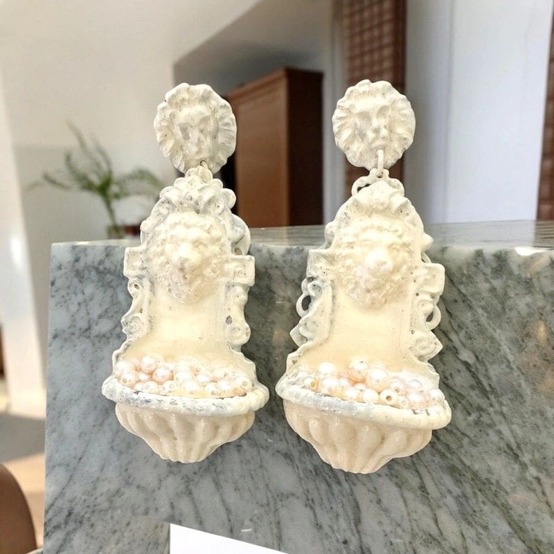A pair of white wall mounted urns with lions heads.