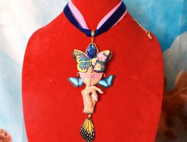 A red mannequin wearing a necklace with a butterfly and angel design.
