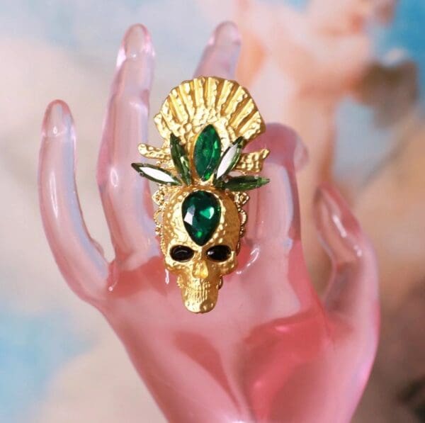 A hand holding a gold mask with green stones.