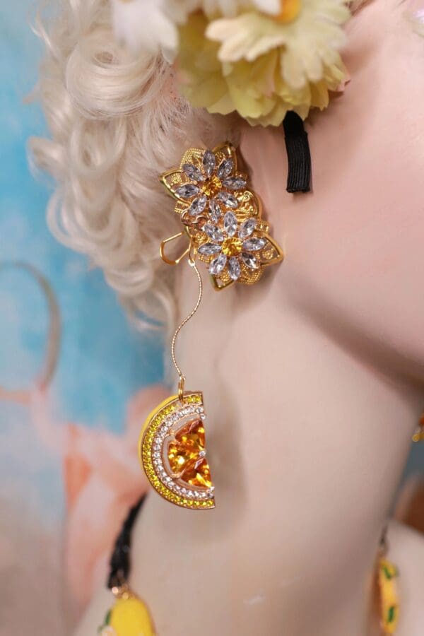 A woman with blonde hair wearing earrings and a yellow flower.