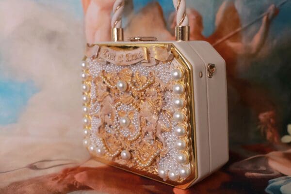 A white purse with gold and pearls on it.