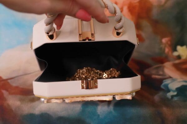 A person opening up a white purse with gold jewelry inside.
