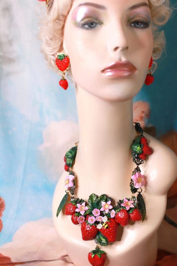 A mannequin wearing a necklace and earrings with strawberries.