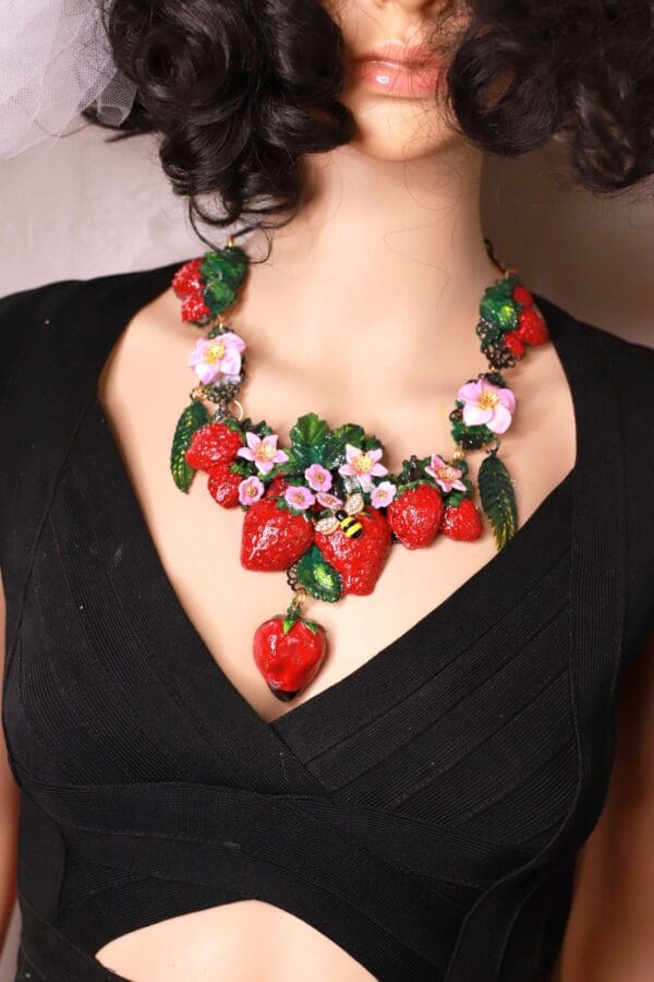 A woman wearing a necklace with strawberries and flowers.