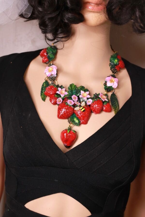 A woman wearing a necklace with strawberries and flowers.