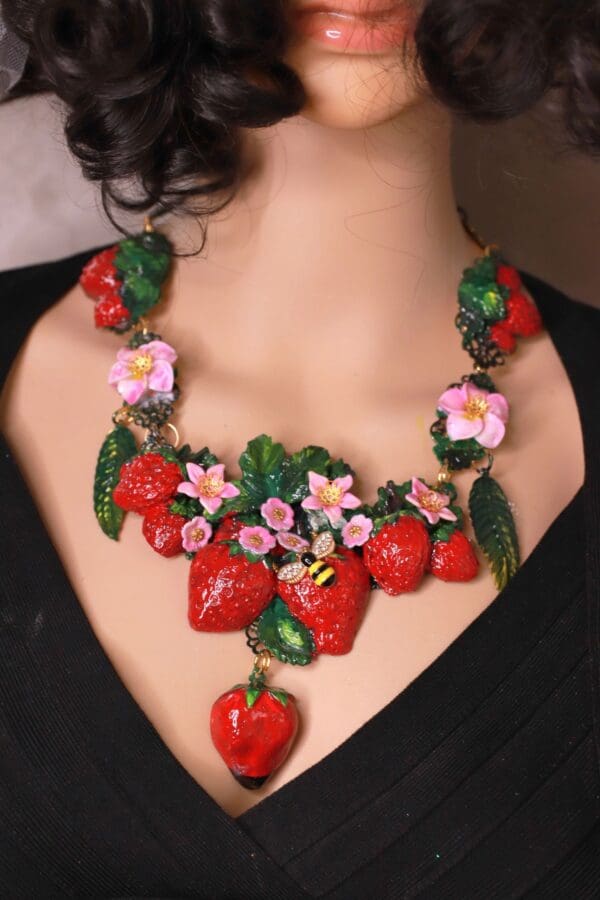 A woman wearing a necklace with strawberries and flowers.