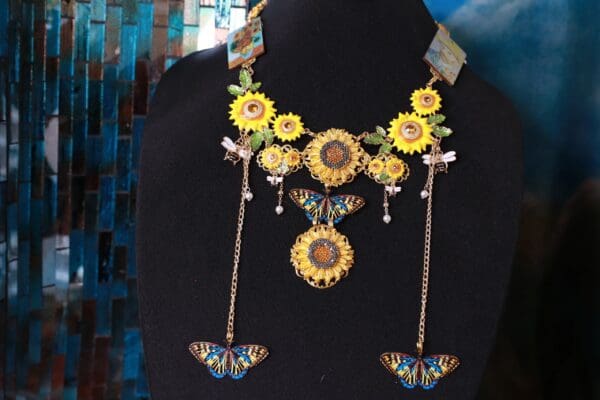 A black mannequin wearing a necklace with sunflowers and butterflies.