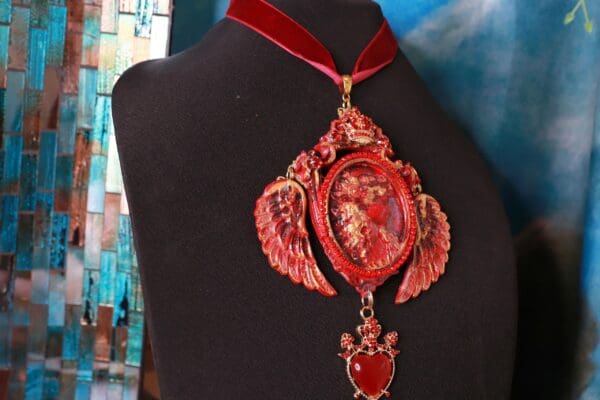 A red necklace with a heart and angel wings.