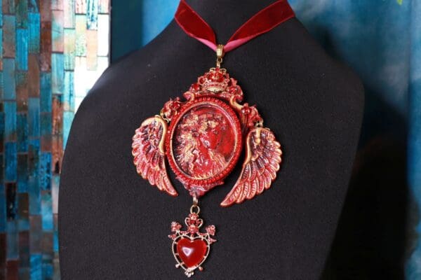 A red necklace with a heart and angel wings.