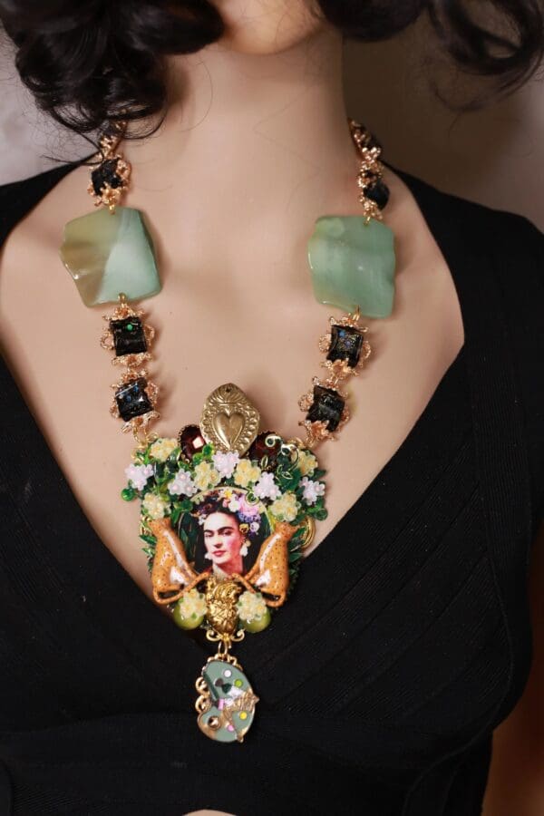 A woman wearing a necklace with green stones and a picture of frida kahlo.