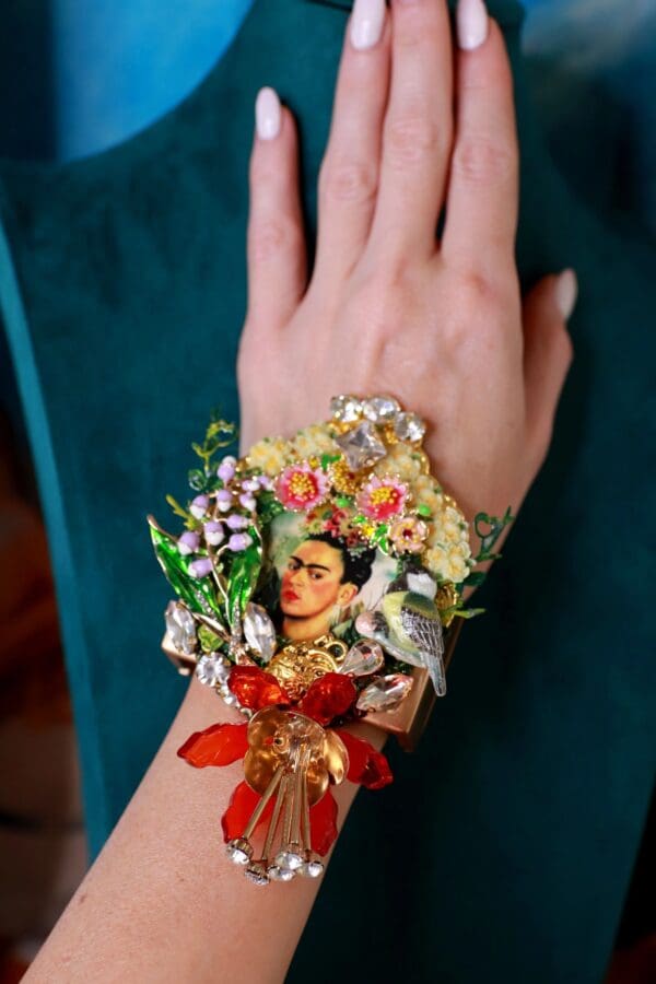 A woman 's hand wearing a bracelet with flowers and a picture of frida kahlo.